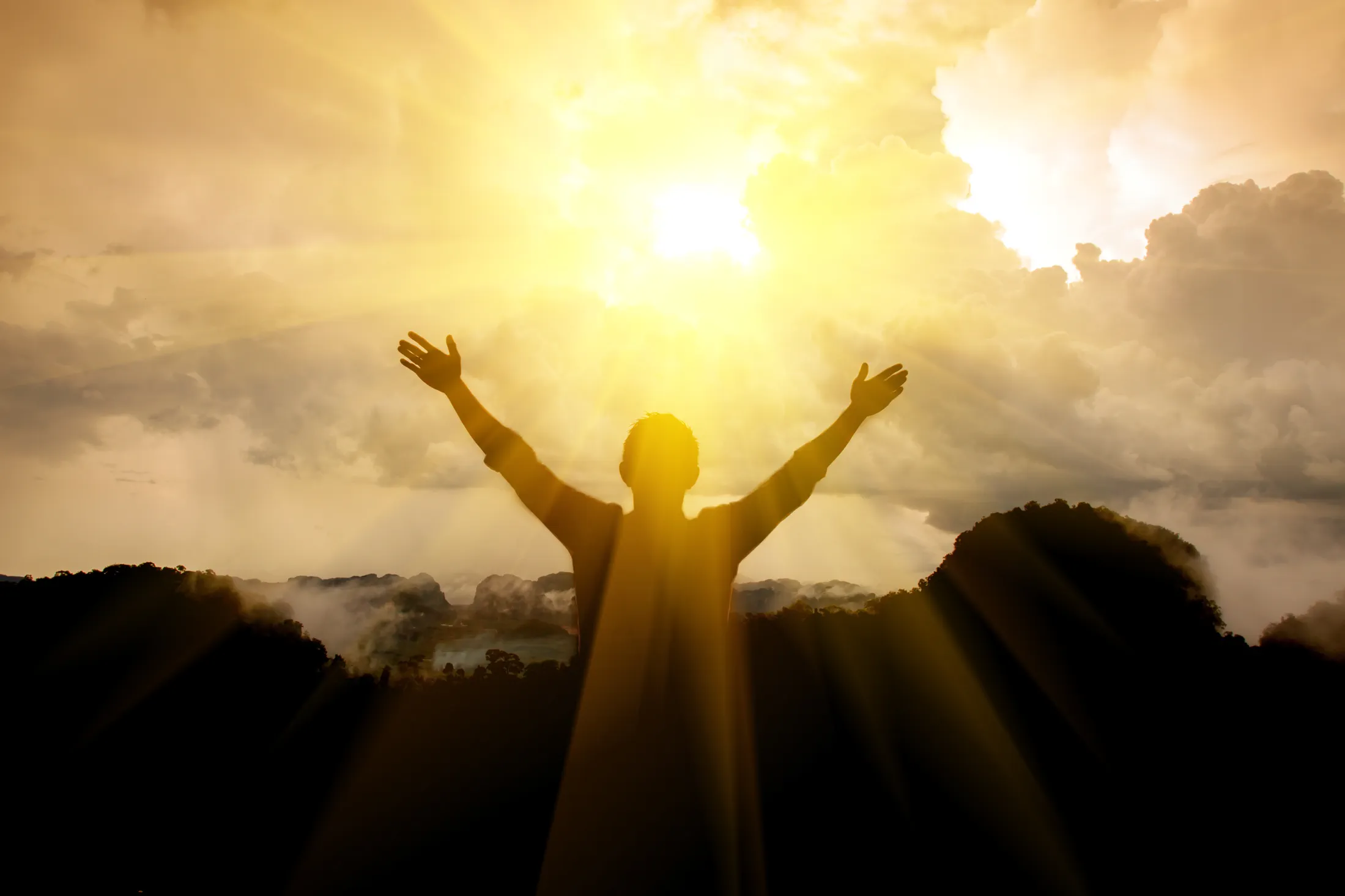 A person standing with arms open toward the sun